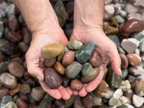 Two hands holding Montana rainbow drain rock